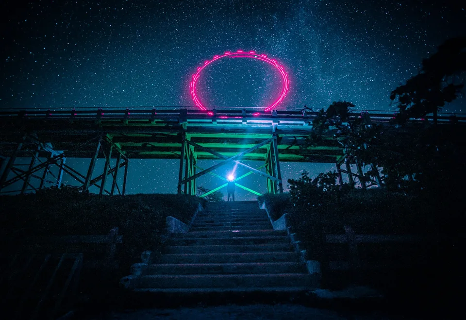 A glowing pink ring frames a starry sky above a bridge at night.